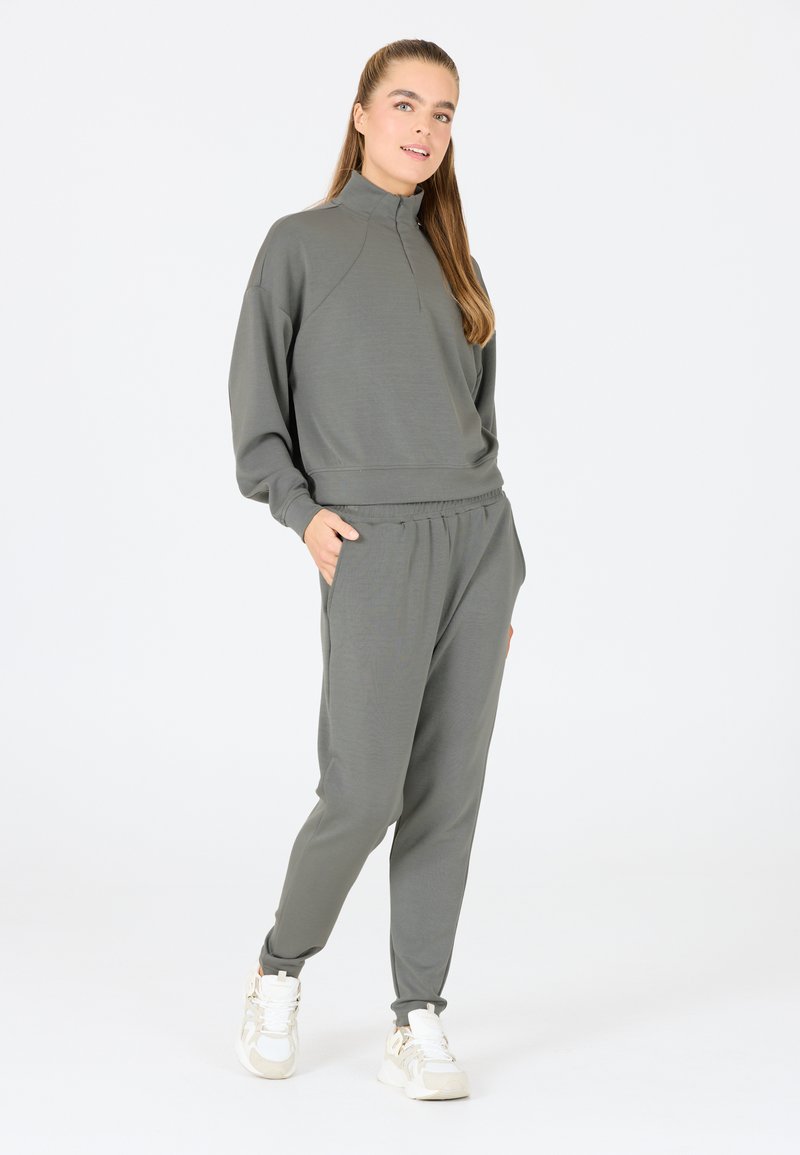 Grijze, lange mouwen pullover met een halve ritssluiting, gecombineerd met bijpassende joggers; gladde textuur met elastische tailleband en zakken.
