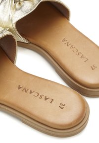 Gold metallic sandals with soft leather straps, tan insoles, and embossed branding detail, featuring a simple design and rounded sole.