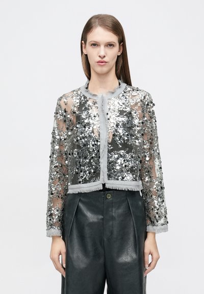 Cropped, sheer jacket with silver sequins and gray trim. Features a round neckline and fringe accents. Paired with black leather trousers.