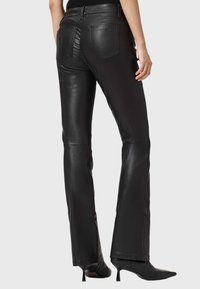 Czarne, skórzane spodnie dzwony o gładkiej fakturze, z tylnymi kieszeniami i przeszyciami, zestawione z czarnymi, spiczastymi szpilkami.