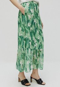 Blomstret maxi-nederdel i gennemsigtig grøn stof med hvide cala-liljer og grønne blade. Har et tieret design og sidelommer.