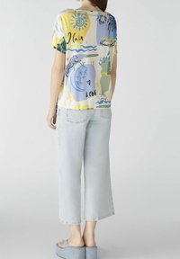 Camicia a maniche corte gialla con motivo a design astratti in blu e verde. Abbinata a jeans in denim chiaro a gamba larga e sandali con zeppa.