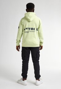 Felpa verde chiaro con testo nero stampato sul retro, abbinata a pantaloni cargo neri e scarpe da ginnastica bianche. Tessuto morbido, design con cappuccio.