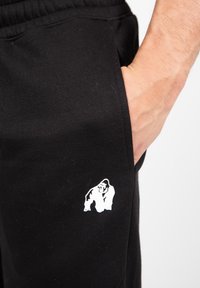 Zwarte sweatpants met een elastische tailleband, voorzien van een wit gorilla-logo op het bovenste deel van de linkerzak. Zachte textuur en casual ontwerp.