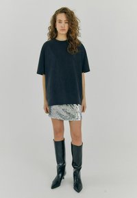 Pārlieku liels tumši zils krekls; sudraba spīguļota mini svārku; melni ceļgalu augstuma augstpapēžu zābaki; modelis ar viļņainiem matiem. Neitrāla fona.