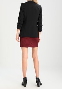 Blazer noir sur mesure à manches longues, associé à une jupe bordeaux. La tenue est complétée par des bottines noires à finition texturée.