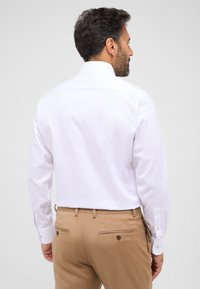Witte blouse met lange mouwen met een gestructureerd patroon, voorzien van een standaard kraag en knoopmouwen, gecombineerd met beige broek.