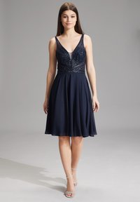 Abito A-line blu navy con corpetto aderente decorato con perline e scollatura a V. Gonna fluida realizzata in materiale leggero, abbinata a tacchi a stiletto argento.