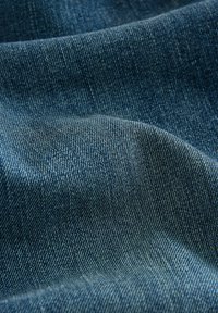 Tmavomodrá džínsovina s hladkou textúrou a viditeľným tkaním twill, ktorá predvádza jemné draping a subtílne farebné variácie.