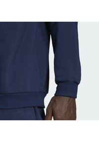 Felpa blu navy con tessuto testa di moro, polsini a costine e vestibilità comoda. Cuciture visibili lungo le cuciture. Mano parzialmente visibile.