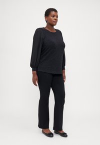 Black textured top with sheer black puff sleeves, paired with fitted black pants and flat black shoes with a bow accent.
