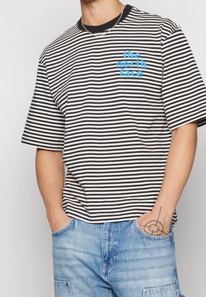 Camiseta de manga corta a rayas en blanco y negro con un logo azul "the north face" en el pecho izquierdo. Material de algodón, corte relajado.