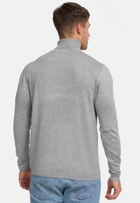 Grauer Langarmpullover aus weichem Strickmaterial, mit hohem Kragen und gerippten Bündchen, kombiniert mit hellblauen Jeans.