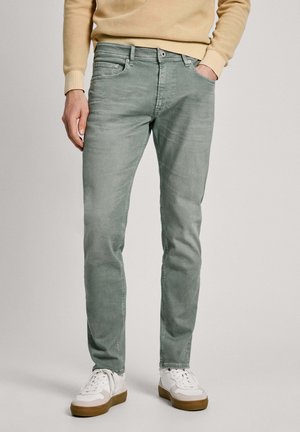 Jean en denim vert avec une coupe slim, doté d'un design à cinq poches et d'un léger effilochage, associés à des baskets blanches.