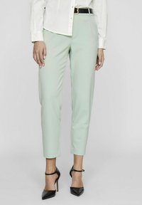Pantalons ajustés vert menthe avec une silhouette slim, dotés d'un devant plat et de coutures discrètes. Portés avec des talons hauts noirs.
