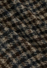 Textúrovaná tkanina v odtieňoch hnedej a béžovej, so vzorom houndstooth a mäkkými, plyšovými povrchovými detailmi.