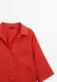 Chemise en lin rouge à boutons avec col, dotée d'une poche avant et de manches courtes. Texture lisse et coupe décontractée.