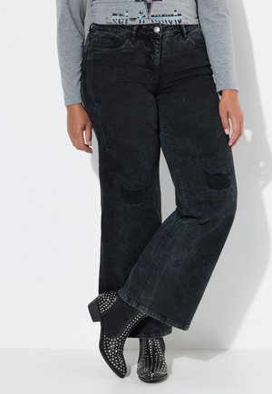 Zwarte denim jeans met wijde pijpen, versierd met gescheurde kniestukken en een middelhoge taille. Gepaarde met zwarte enkellaarsjes met studs.