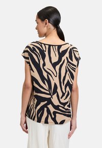 T-shirt à manches courtes en tissu beige, arborant un motif de feuilles abstraites noires, avec un col rond et une coupe décontractée, dotée d'une ligne d'ourlet droite.