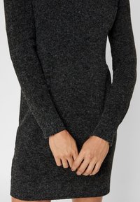 Robe en tricot gris foncé, dotée de manches longues et d'une silhouette ajustée. Tissu texturé avec une finition douce et un motif subtil.
