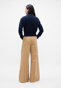 Námornícky pletený sveter s golierom, kombinovaný s béžovými nohavicami s širokými nohavicami. Sveter má textúrovanú tkaninu a skrátený strih.