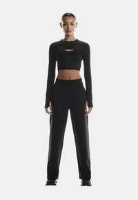 Black cropped long-sleeve top with keyhole detail, paired with loose-fitting black sweatpants. Soft, smooth fabric with minimal accents.