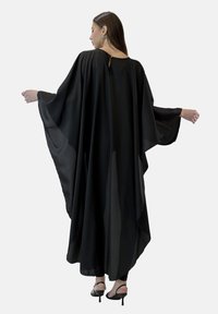 Czarny kaftan z luźnymi, przezroczystymi rękawami i delikatnym dołem wyższym z przodu. Posiada wycięcie w kształcie łezki z tyłu. Wykonany z lekkiego materiału.