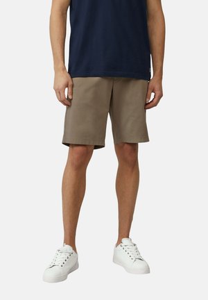 Shorts kaki avec une coupe décontractée, fabriqués en tissu lisse. Associés à des baskets blanches, au design simple et à la fermeture à lacets.