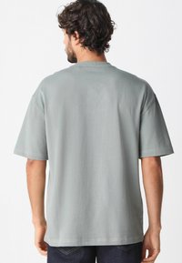 Lys grå bomulds t-shirt med korte ærmer, en afslappet pasform og rund halsudskæring. Søm detaljer langs skuldrene og kanten.