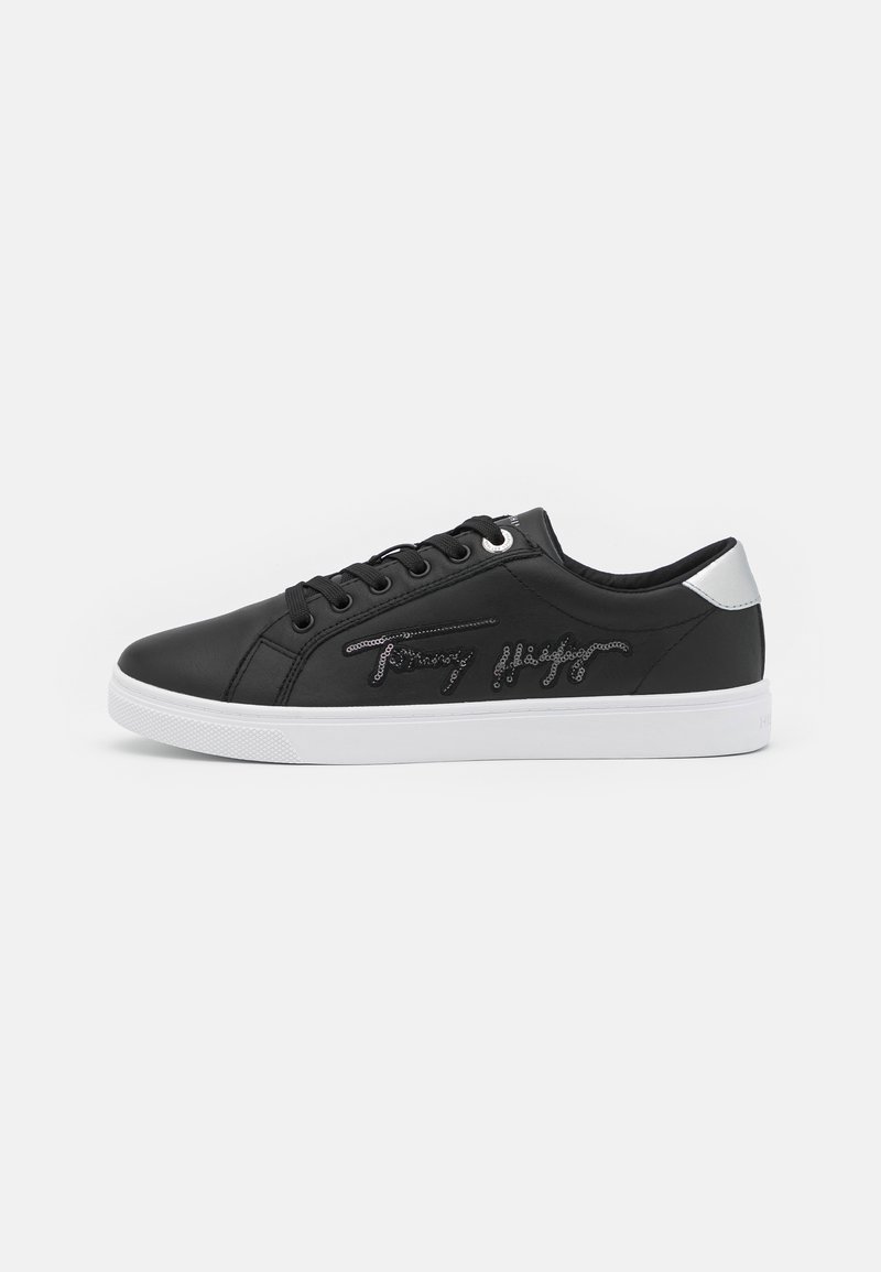 Baskets basses noires avec semelle blanche et languette au talon, lacets devant et logo de la marque brodé sur le côté.