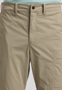 Beige Cargo-Shorts aus leichtem Material, mit einem Reißverschluss und seitlichen Taschen. Die Textur ist glatt mit einem dezenten, feinen Muster.