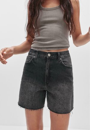 Shorts en denim noir avec un ourlet effiloché, un détail de texture à pois, cinq poches et un fermoir à bouton argenté. Associés à un débardeur gris à côtes.