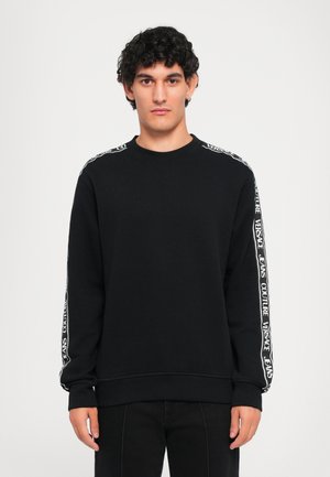 Black sweatshirt made of soft fabric, featuring long sleeves with white logo accents along the shoulders and stretchy cuffs. Round neckline.