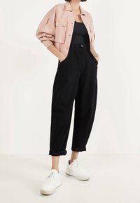 Ljusrosa kort jacka med två bröstfickor, svarta högmidjade byxor med manschetter, och vita sneakers med texturerade sulor.