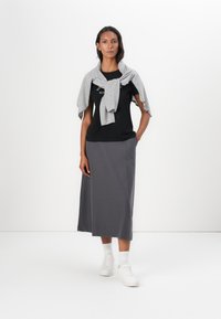 Tricou negru cu text, pulover gri legat la gât și fustă midi gri. Tenisi albi completează ținuta. Texturi netede în întreaga alcătuire.