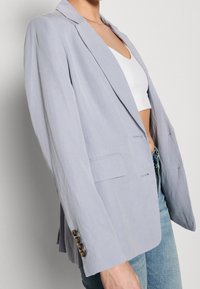 Jasnoszara lniana marynarka z klapami z wycięciami, dwoma guzikami i bocznymi kieszeniami, z trzema guzikami na mankietach.