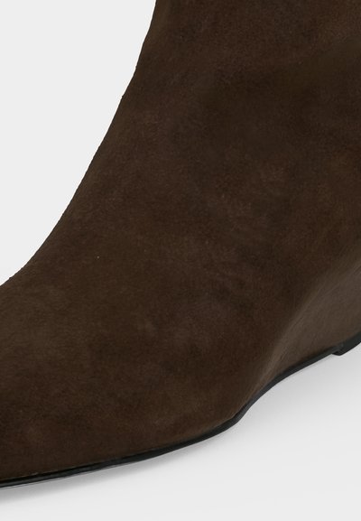 Gros plan sur l’avant d’une botte cheville en daim marron avec un bout légèrement pointu et une semelle plate noire.