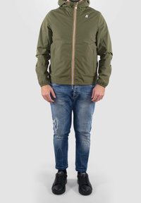 Olivgrüne Kapuzenjacke mit einem Frontreißverschluss, elastischen Bündchen und zwei Seitentaschen, kombiniert mit zerrissenen blauen Jeans und schwarzen Turnschuhen.