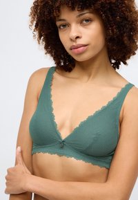 Bralette verde texturizado com bordas onduladas e um pequeno botão ao centro. Alças ajustáveis e um decote em V.