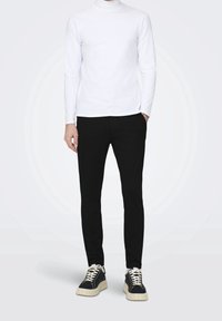 Suéter blanco de cuello alto de manga larga, pantalones negros ajustados y zapatillas negras con suelas texturizadas y acentos crema. Diseño simple y moderno.