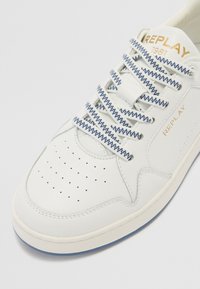 Sneaker bianca in pelle con lacci blu a fantasia, punta perforata e marchio dorato "REPLAY 1981" di lato. Suola in gomma con dettagli blu.
