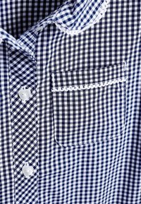 Skjorta med marinblått och vitt rutigt ginghammönster, knäppning framtill, en bröstficka och scalloped kant runt fickan. Bomullstyg.