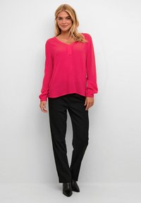 Blusa rosa de manga larga con escote en V y detalle de botones, combinada con pantalones negros a medida y botas de tobillo negras de punta.
