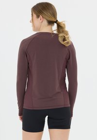 Langærmet, maroon atletisk top med en tætsiddende design og sømløse skuldre, parret med sorte shorts. Glat tekstur, velegnet til aktivt tøj.