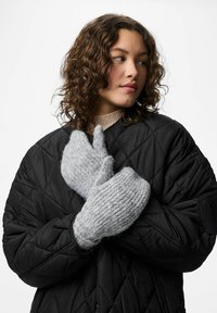 Grå strikkede vanter med en blød, tekstureret afslutning, parret med en sort quiltet jakke. Vanterne er oversized og hyggelige.