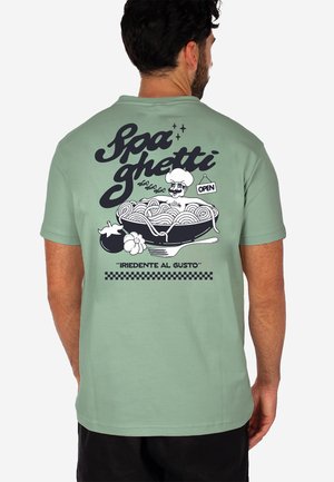Man wearing green T-shirt with cartoon chef in spaghetti bowl, text "Spaghetti" and "Iriedente al Gusto" on the back.