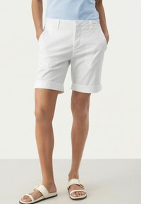 Shorts bianchi in cotone con risvolti, due tasche laterali e design affusolato, abbinati a sandali leggeri con una fibbia decorativa.