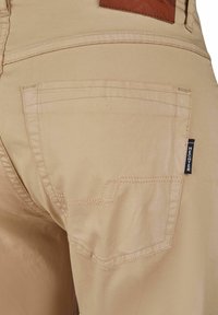 Beige broek met een gladde textuur en gestikte accenten. Voorzien van een achterzak met een merklabel en een leren patch erboven.