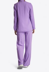 Liliowy garnitur z marynarką na jeden guzik i spodniami o szerokich nogawkach, gładka faktura, lekko dopasowany krój i minimalistyczne detale metalowe.