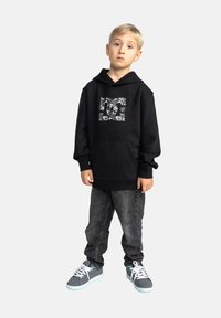 Zwarte hoodie met grafisch ontwerp aan de voorkant, kangoeroezak, geribde manchetten, gecombineerd met donkere spijkerbroek en grijze sneakers met witte veters.
